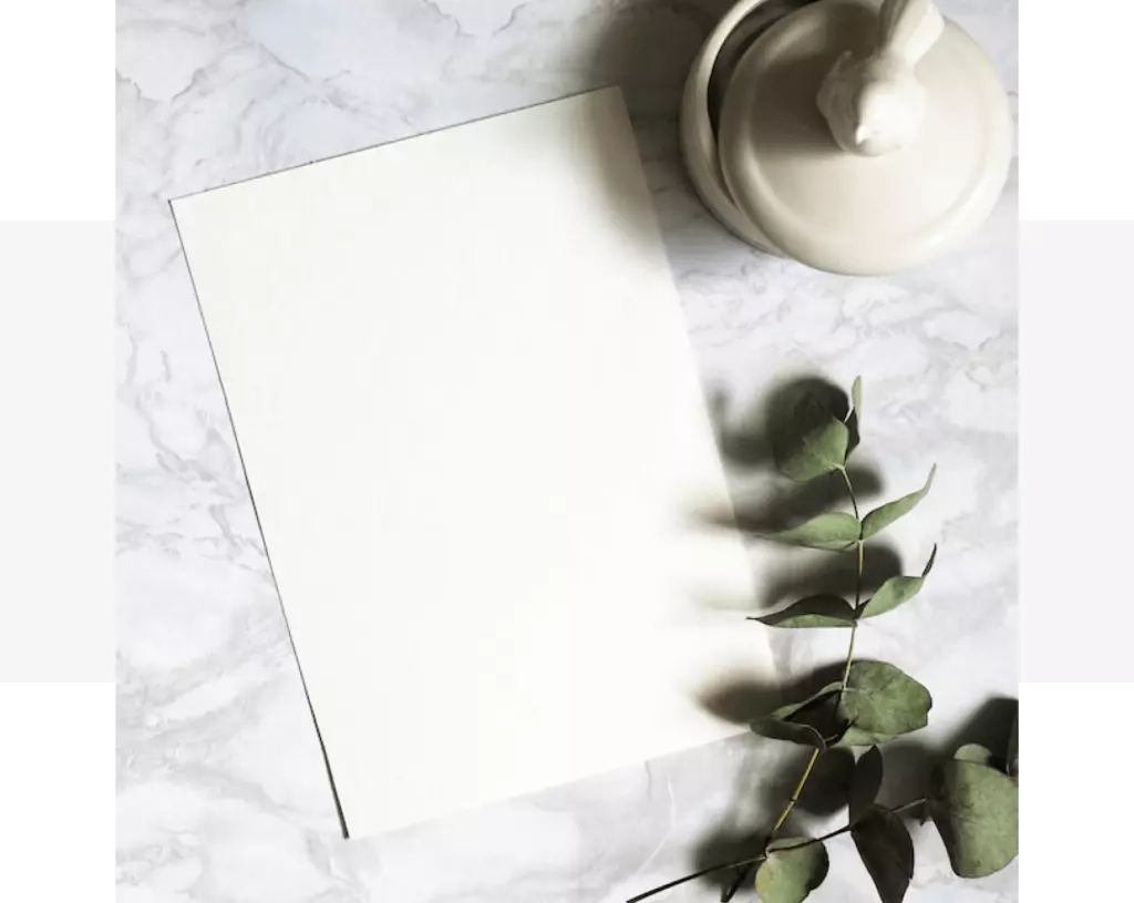 A white paper on a marble table with eucalyptus leaves featuring White Quartz Benchtops.