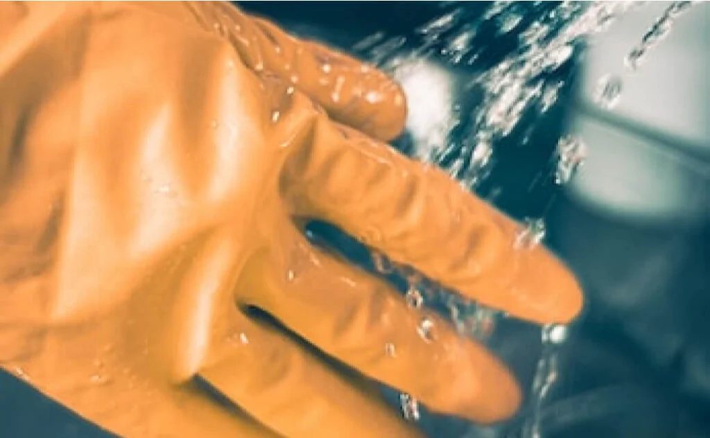 A person wearing rubber gloves is washing their hands with water.